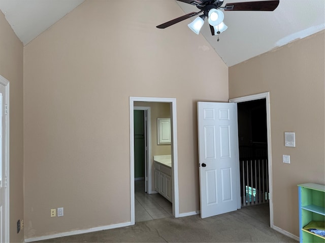 unfurnished bedroom featuring light carpet, ceiling fan, ensuite bathroom, high vaulted ceiling, and a walk in closet