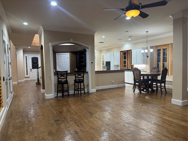 kitchen featuring ceiling fan with notable chandelier, a kitchen bar, dark wood-type flooring, white cabinetry, and ornamental molding