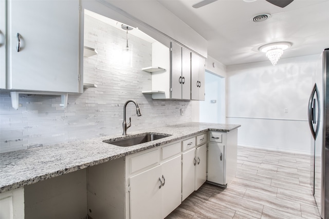 kitchen with stainless steel fridge, white cabinetry, sink, and hanging light fixtures