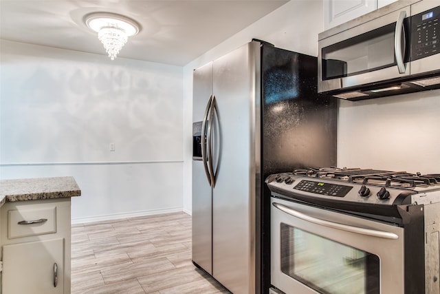 kitchen featuring an inviting chandelier, white cabinets, light hardwood / wood-style floors, light stone counters, and stainless steel appliances