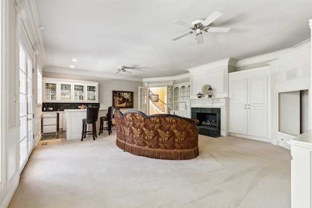 carpeted living room featuring ceiling fan, a tiled fireplace, and ornamental molding