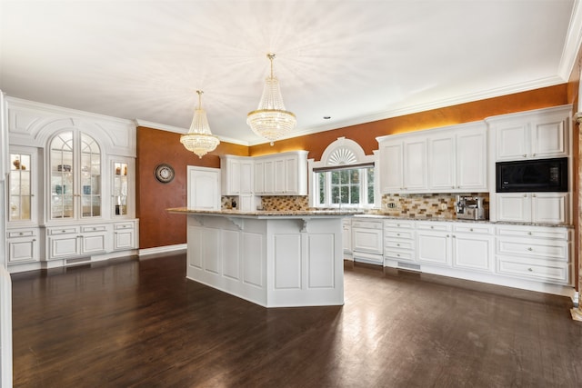 kitchen featuring black microwave, an inviting chandelier, white cabinets, a kitchen island, and decorative light fixtures