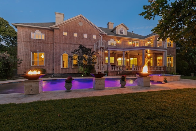 back house at dusk with a lawn, a balcony, and a patio