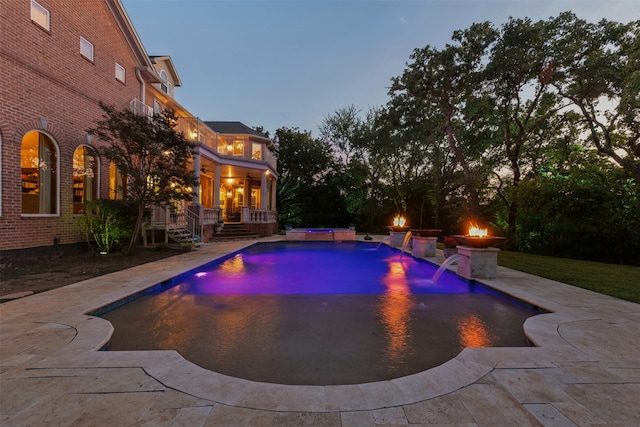 pool at dusk featuring a patio, an outdoor fire pit, and pool water feature