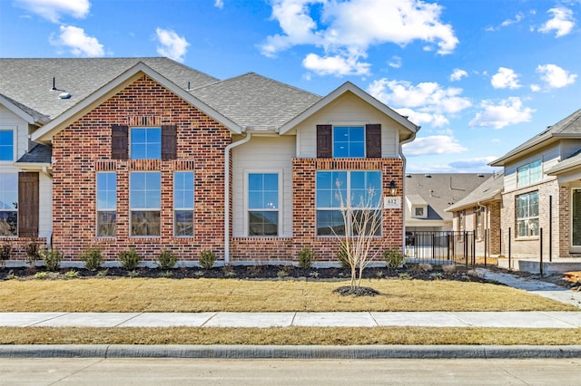 traditional home featuring a shingled roof, brick siding, and a front lawn