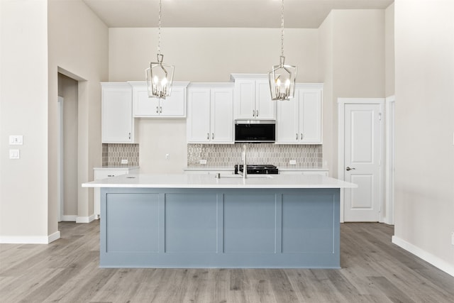 kitchen with white cabinetry, stainless steel microwave, a kitchen island with sink, and an inviting chandelier