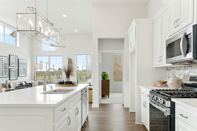 kitchen featuring appliances with stainless steel finishes, decorative light fixtures, sink, an island with sink, and white cabinets