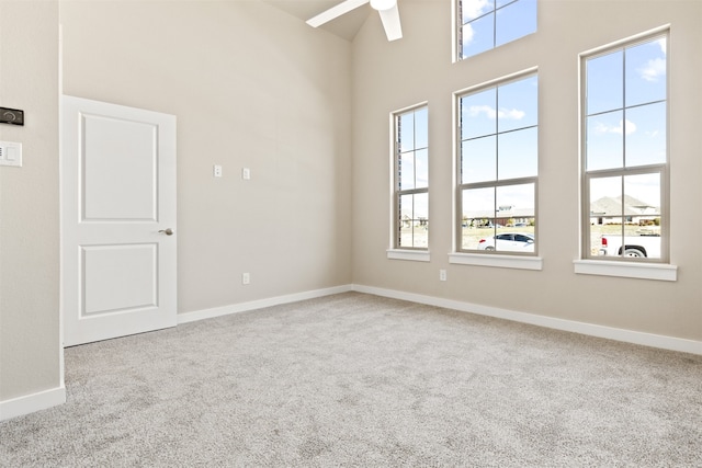 carpeted empty room with baseboards, ceiling fan, a high ceiling, and a healthy amount of sunlight