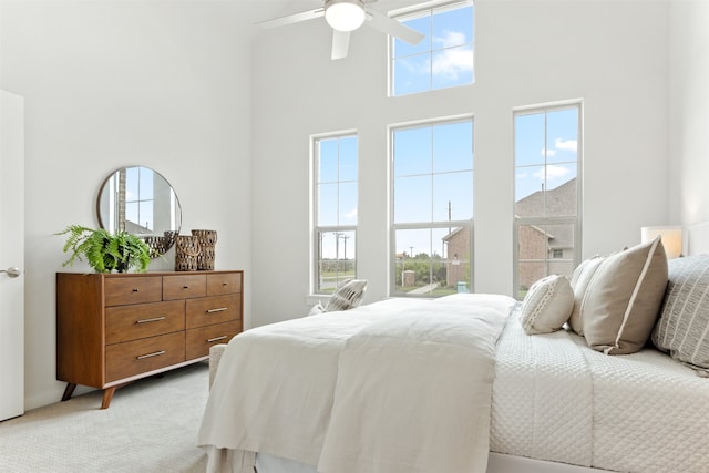 bedroom featuring a towering ceiling, multiple windows, light colored carpet, and ceiling fan