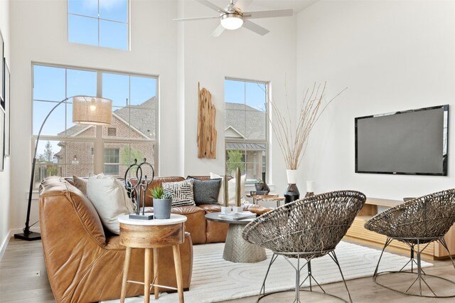 living room with ceiling fan, a towering ceiling, a healthy amount of sunlight, and light hardwood / wood-style flooring