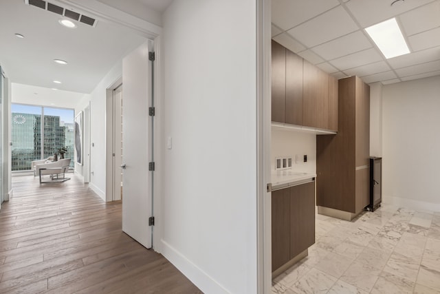 hallway featuring floor to ceiling windows, light hardwood / wood-style flooring, and a paneled ceiling