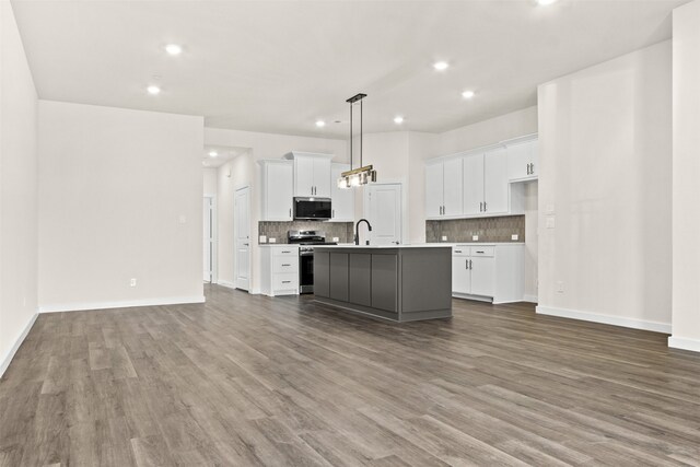 kitchen with appliances with stainless steel finishes, decorative light fixtures, light hardwood / wood-style floors, white cabinets, and a kitchen island with sink