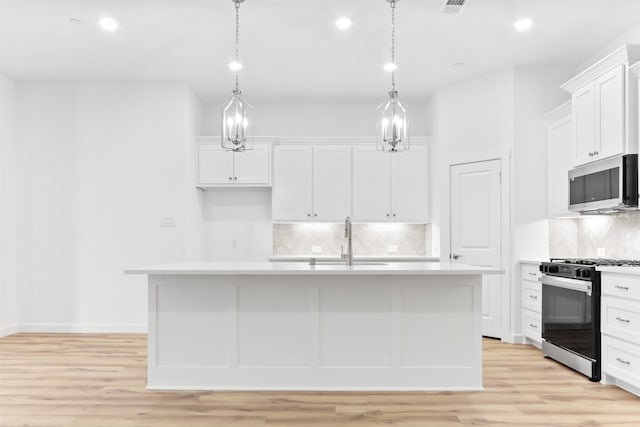 kitchen featuring white cabinetry, stainless steel appliances, hanging light fixtures, and an island with sink