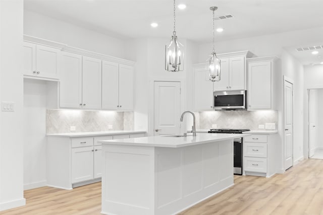 kitchen featuring light wood-type flooring, appliances with stainless steel finishes, an island with sink, and white cabinets