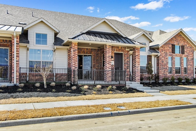 townhome / multi-family property with metal roof, a porch, brick siding, a shingled roof, and a standing seam roof