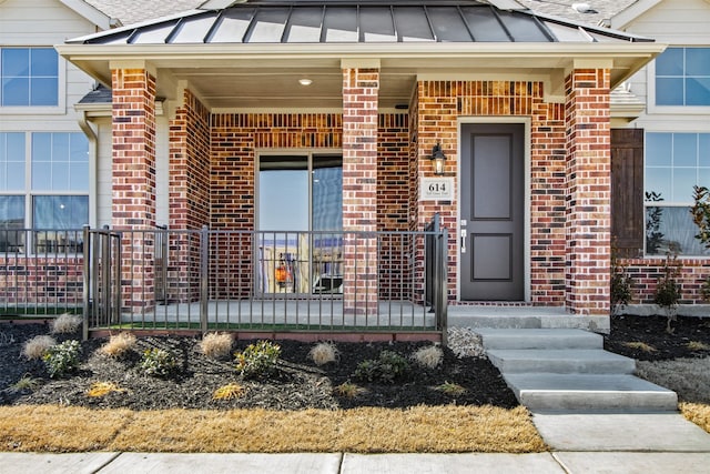 entrance to property featuring a standing seam roof, a porch, and brick siding