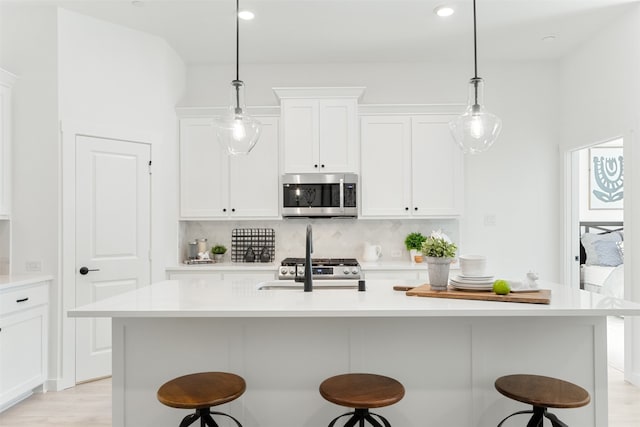 kitchen featuring stainless steel appliances, a kitchen bar, pendant lighting, an island with sink, and white cabinets