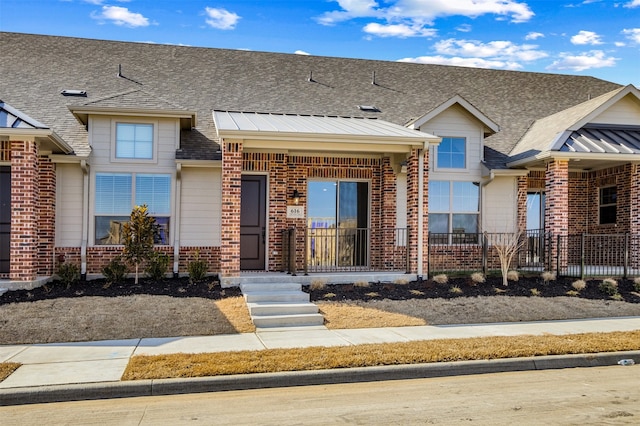 view of property with a standing seam roof, metal roof, brick siding, and roof with shingles