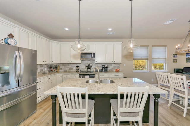 kitchen with white cabinetry, light stone counters, decorative light fixtures, appliances with stainless steel finishes, and a kitchen island with sink