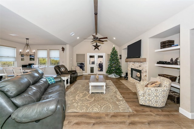 living room with a stone fireplace, hardwood / wood-style floors, lofted ceiling with beams, and ceiling fan with notable chandelier