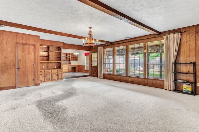 unfurnished living room with an inviting chandelier, wooden walls, a textured ceiling, and beam ceiling