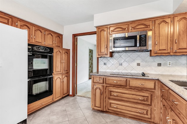 kitchen with black appliances, tasteful backsplash, light stone counters, light tile patterned flooring, and a textured ceiling