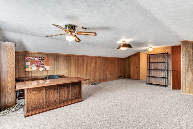 interior space featuring a textured ceiling, wood walls, vaulted ceiling, light colored carpet, and ceiling fan