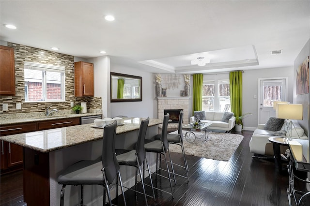 kitchen featuring dark hardwood / wood-style flooring, a center island, a raised ceiling, and a stone fireplace