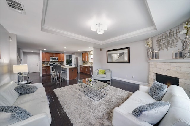 living room featuring ornamental molding, dark hardwood / wood-style floors, a raised ceiling, and a stone fireplace