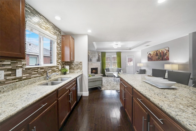 kitchen with sink, light stone counters, stainless steel dishwasher, dark hardwood / wood-style floors, and a fireplace