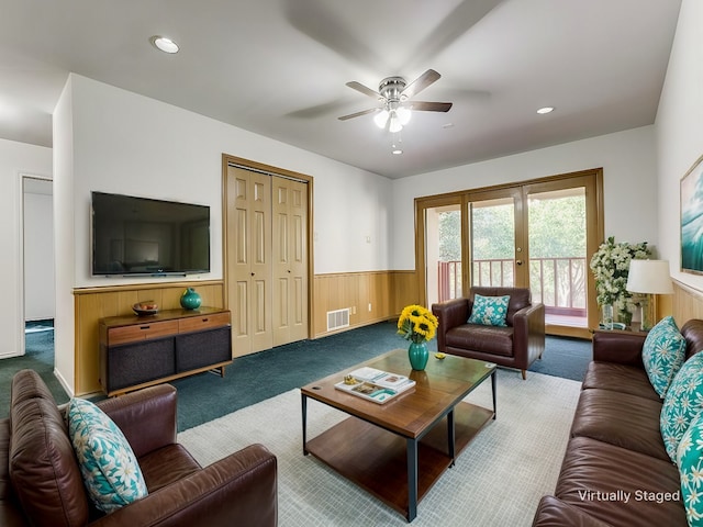 carpeted living room featuring wooden walls and ceiling fan