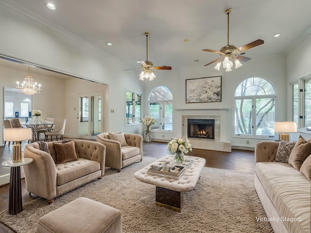 living room featuring ceiling fan with notable chandelier, hardwood / wood-style flooring, crown molding, and a tiled fireplace