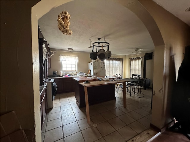 kitchen featuring dark brown cabinetry, crown molding, light tile patterned floors, a kitchen island, and ceiling fan