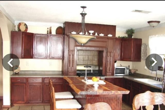 kitchen with sink, crown molding, hanging light fixtures, a kitchen island with sink, and stove