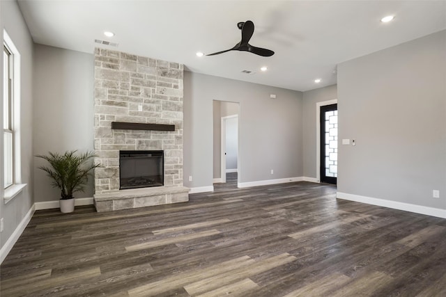 unfurnished living room with a stone fireplace, ceiling fan, a healthy amount of sunlight, and dark hardwood / wood-style floors