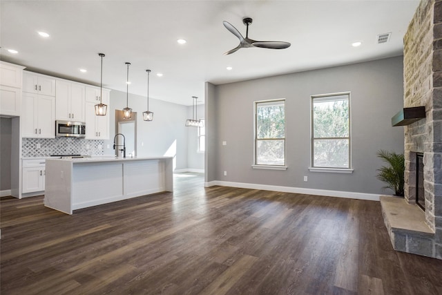 kitchen with a stone fireplace, a kitchen island with sink, white cabinetry, and pendant lighting