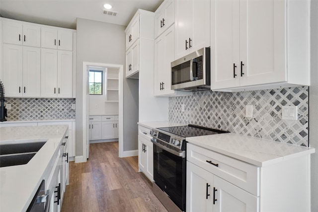 kitchen with wood-type flooring, light stone counters, decorative backsplash, white cabinetry, and appliances with stainless steel finishes