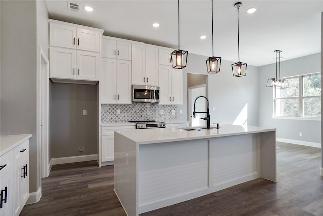 kitchen with a kitchen island with sink, appliances with stainless steel finishes, dark wood-type flooring, and decorative light fixtures