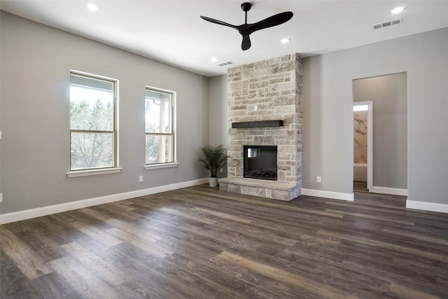 unfurnished living room featuring dark wood-type flooring, a stone fireplace, and ceiling fan