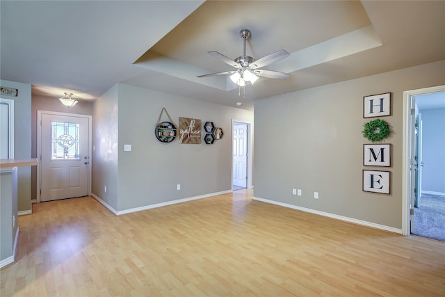 entrance foyer with light wood-type flooring, a tray ceiling, and ceiling fan