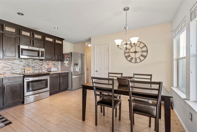 kitchen with stainless steel appliances, an inviting chandelier, dark brown cabinetry, light wood-type flooring, and decorative light fixtures