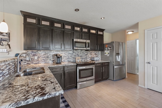 kitchen featuring light stone counters, stainless steel appliances, backsplash, decorative light fixtures, and sink