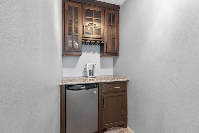 bar with dark brown cabinets, stainless steel appliances, and light stone countertops