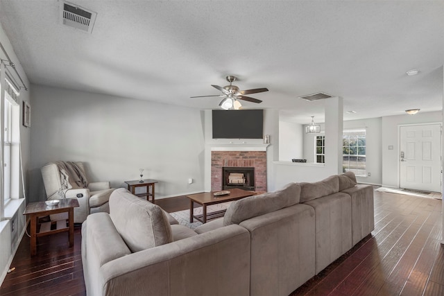 living room with a brick fireplace, dark hardwood / wood-style flooring, a textured ceiling, and ceiling fan