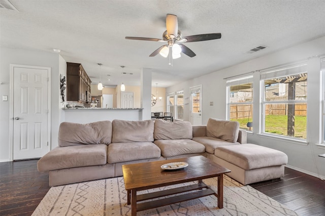 living room featuring dark wood-type flooring, ceiling fan with notable chandelier, and a textured ceiling