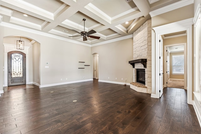 unfurnished living room featuring beamed ceiling, dark hardwood / wood-style floors, a stone fireplace, crown molding, and coffered ceiling