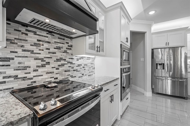 kitchen with stainless steel appliances, light stone countertops, wall chimney exhaust hood, white cabinets, and decorative backsplash