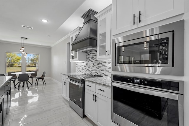 kitchen featuring light stone counters, white cabinets, decorative backsplash, appliances with stainless steel finishes, and premium range hood