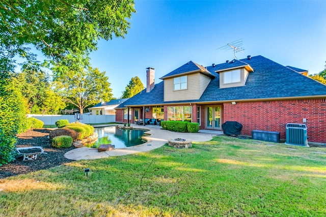 rear view of property with a yard, a fenced in pool, an outdoor fire pit, and central air condition unit