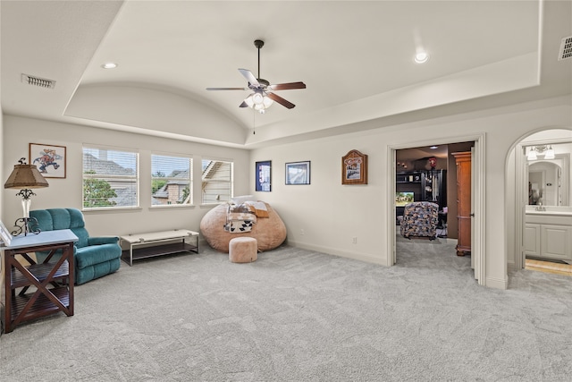 living area with a tray ceiling, lofted ceiling, light colored carpet, and ceiling fan